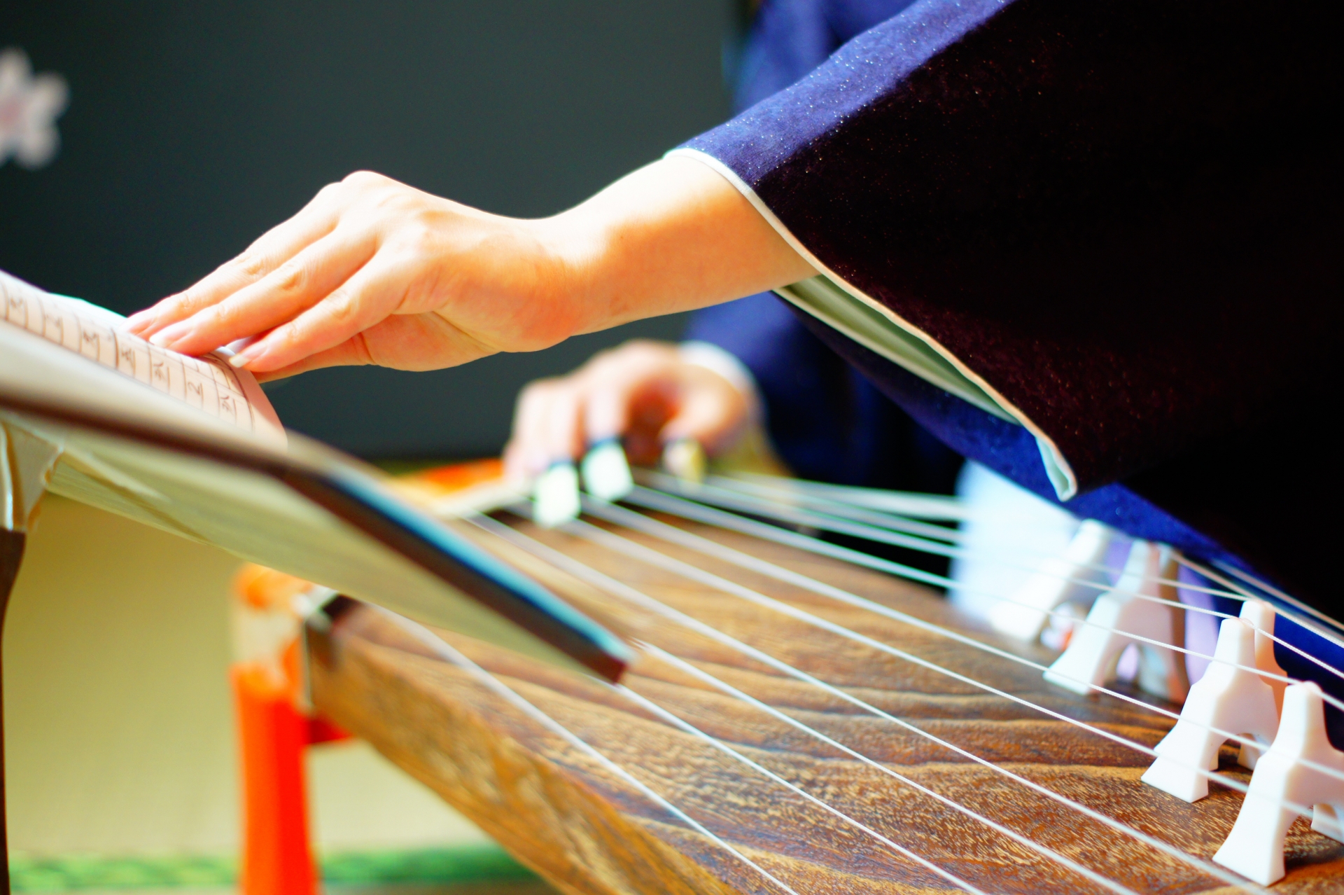Hands playing a Japanese koto while reading traditional sheet music
