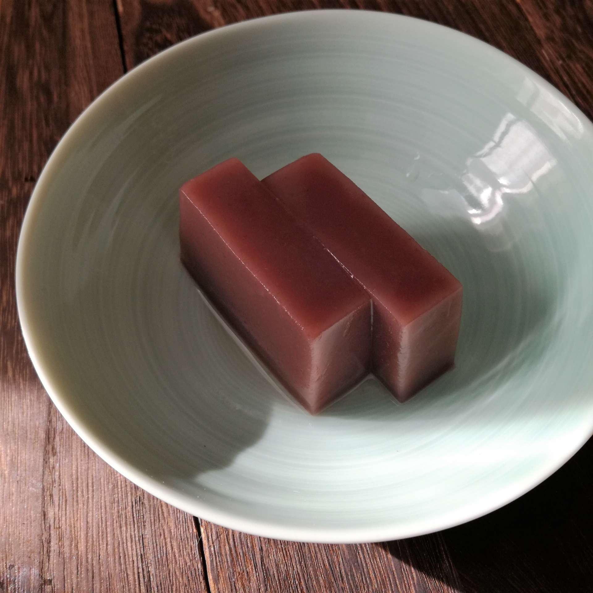 Two pieces of smooth seasonal yokan resting in a pale celadon bowl, illuminated by gentle natural light.